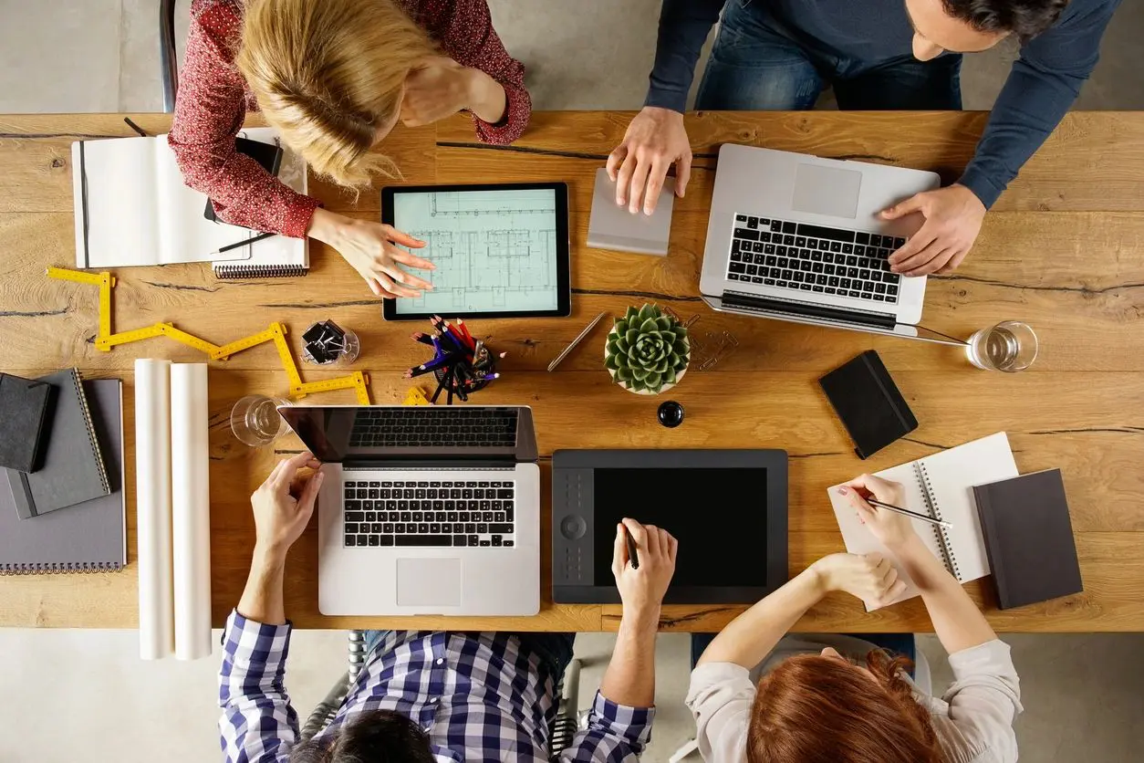 A group of people sitting around a table with laptops.