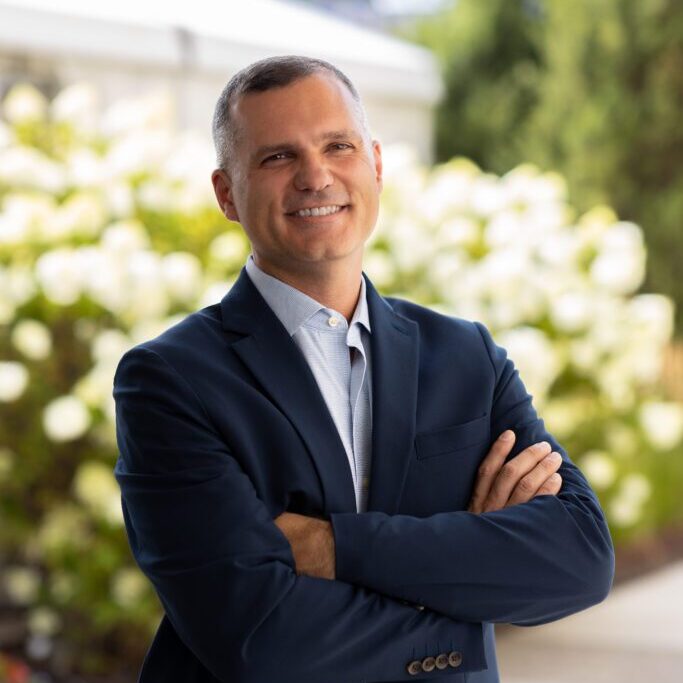 Smiling man in suit, arms crossed.