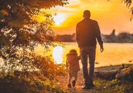 A man and child walking on the beach at sunset.