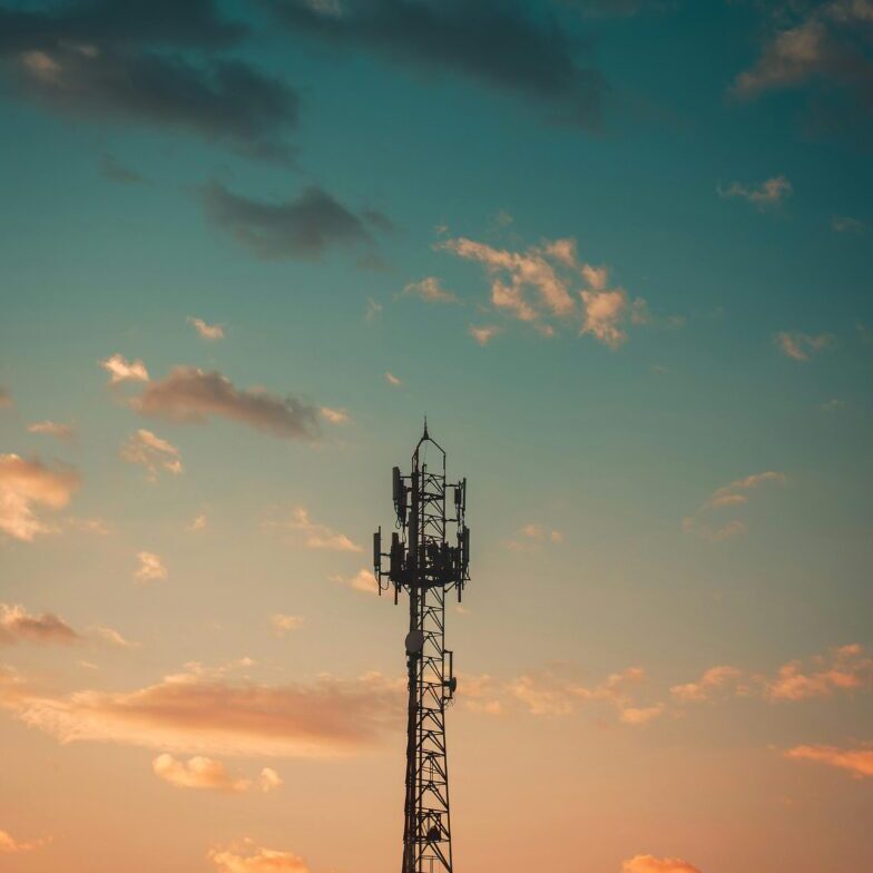 A cell phone tower with the sun setting in the background.